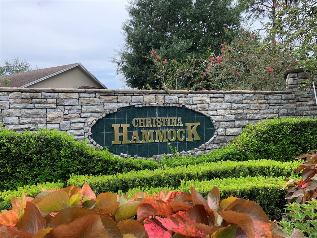 A stone wall features an oval sign reading Christina Hammock behind manicured hedges and plants — 6560 LAKE CLARK DRIVE, LAKELAND, FL