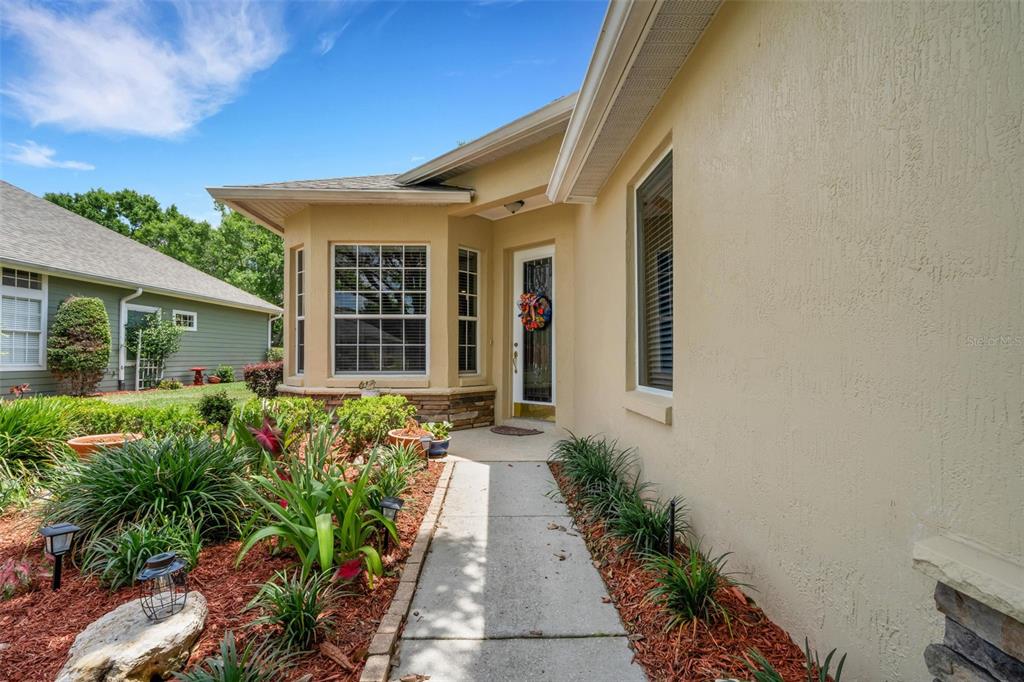 A concrete walkway leads to the front entrance of a tan house with a bay window — 6560 LAKE CLARK DRIVE, LAKELAND, FL