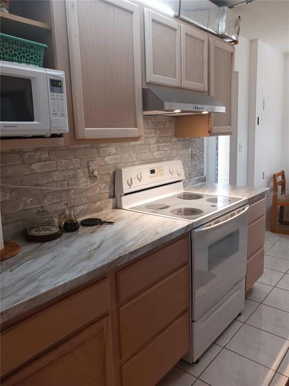 A kitchen features light wood cabinets, a white stove, and a faux-brick backsplash — 2901 NW 48TH AVENUE UNIT 367, LAUDERDALE LAKES, FL