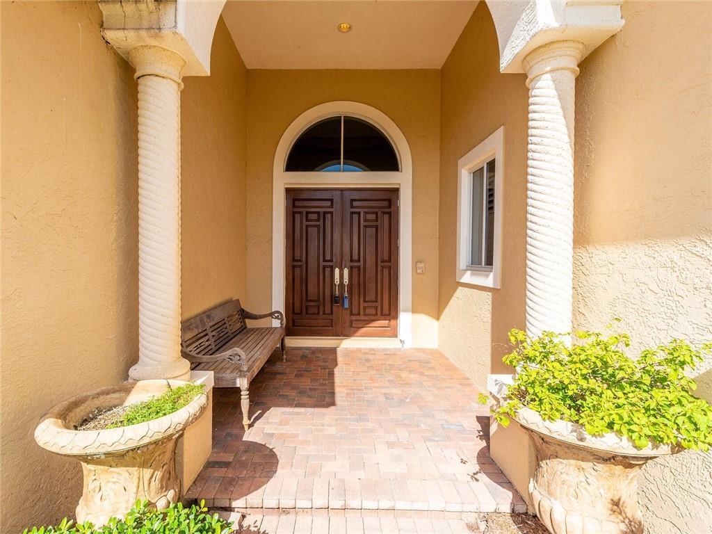 A covered entryway features double wooden doors, two decorative columns, and a brick-paved floor — 775 Greensward Lane, Delray Beach FL 33445, DELRAY BEACH, FL