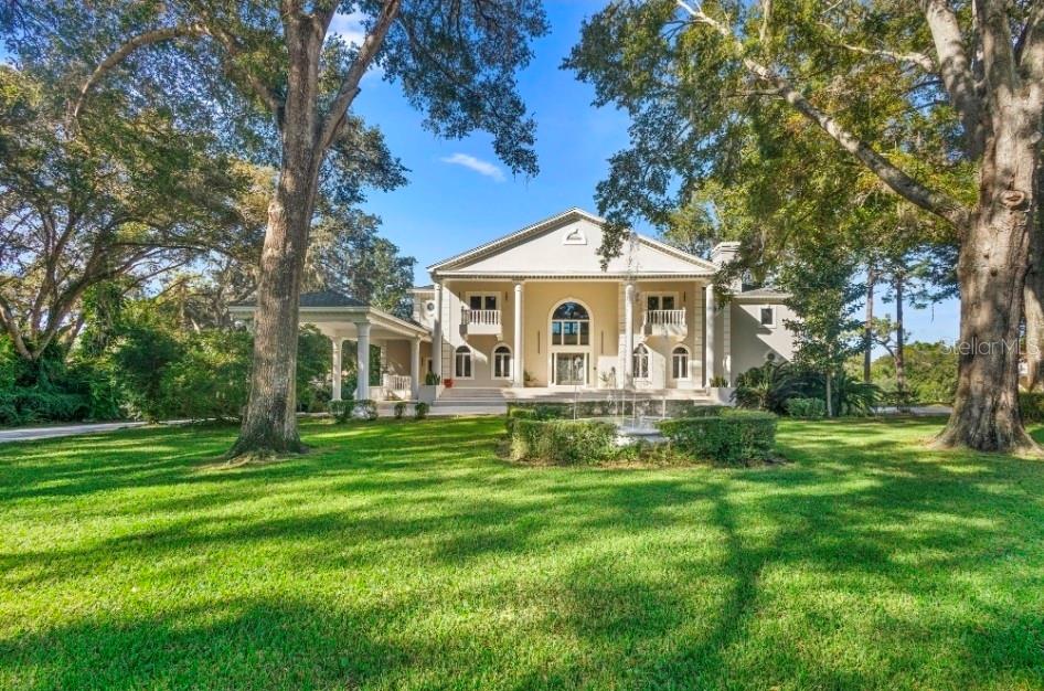 A large, two-story neoclassical home with a front portico and fountain sits on a lawn — 1126 BROWNSHIRE COURT, LONGWOOD, FL