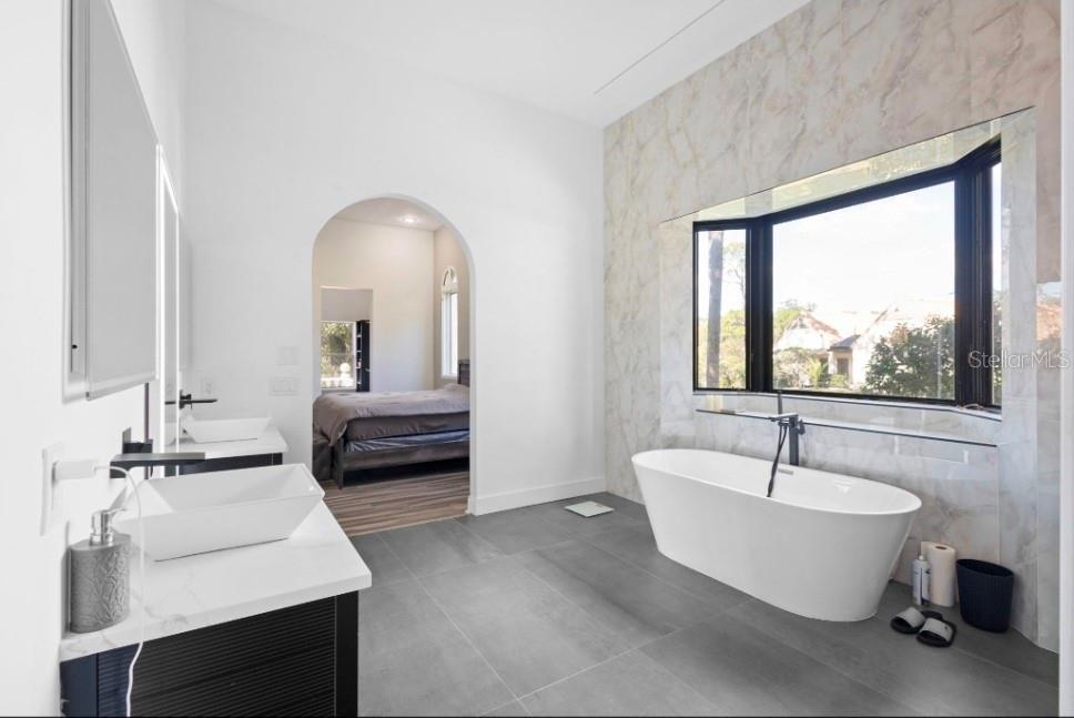 A modern bathroom features a freestanding tub, dual vessel sinks, and a large arched doorway — 1126 BROWNSHIRE COURT, LONGWOOD, FL