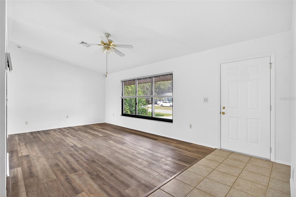 An empty living room features wood-look flooring, white walls, a ceiling fan, and a front door — 141 AVENS STREET, PORT CHARLOTTE, FL