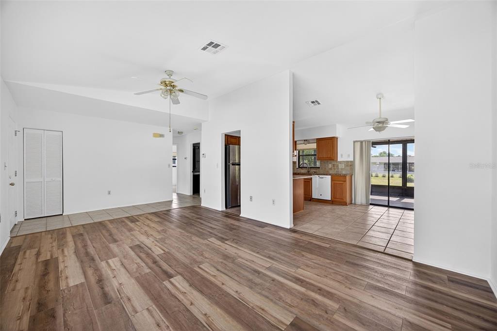 A living room with wood-look flooring leads into a tiled kitchen and dining area — 141 AVENS STREET, PORT CHARLOTTE, FL