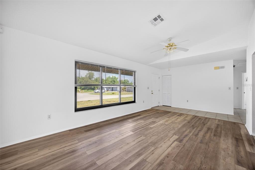 A living room with wood-look flooring, white walls, a ceiling fan, and a large window — 141 AVENS STREET, PORT CHARLOTTE, FL