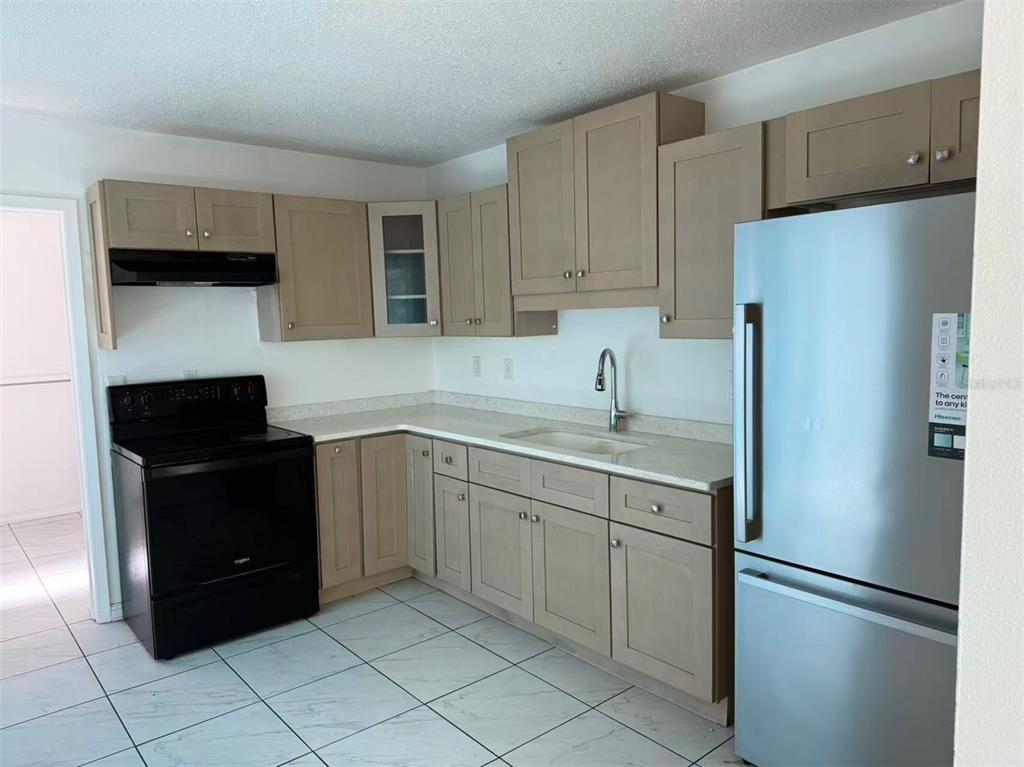 A kitchen features light brown cabinets, white countertops, a black stove, and a stainless refrigerator — 4326 80TH STREET W, BRADENTON, FL