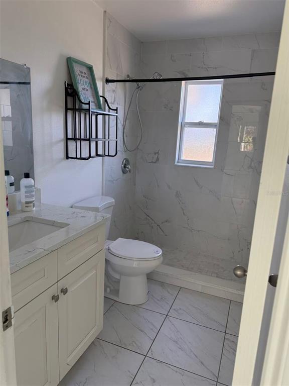 A bathroom features a white vanity, a toilet, and a walk-in shower with marble-look tile — 4326 80TH STREET W, BRADENTON, FL