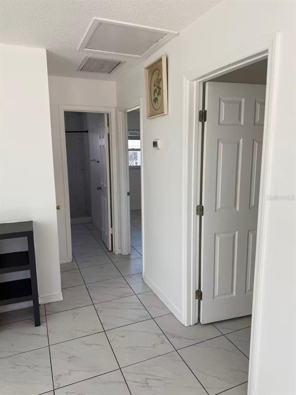 A hallway with white tile floors leads to two open doorways and a closed door — 4326 80TH STREET W, BRADENTON, FL