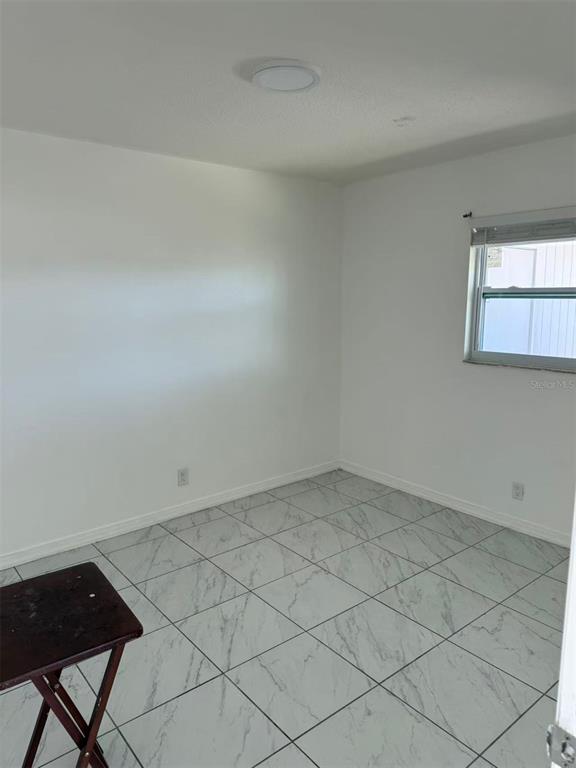 An empty room with white walls, a single window, and white marble-patterned tile flooring — 4326 80TH STREET W, BRADENTON, FL