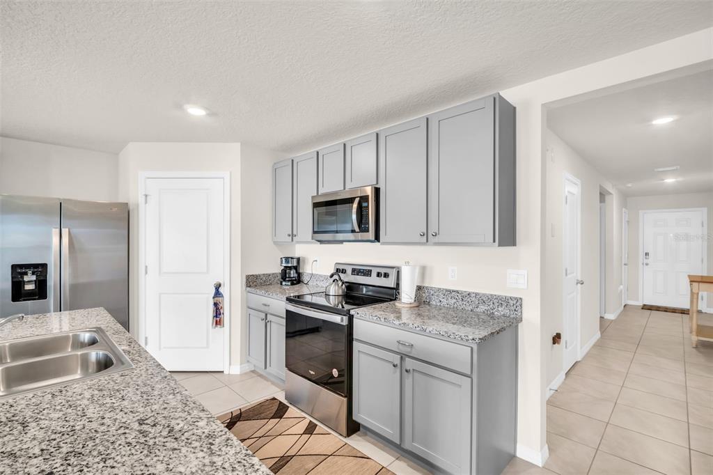 A kitchen features gray cabinets, granite countertops, stainless steel appliances, and tile flooring — 7774 SAIL CLOVER LANE, ZEPHYRHILLS, FL