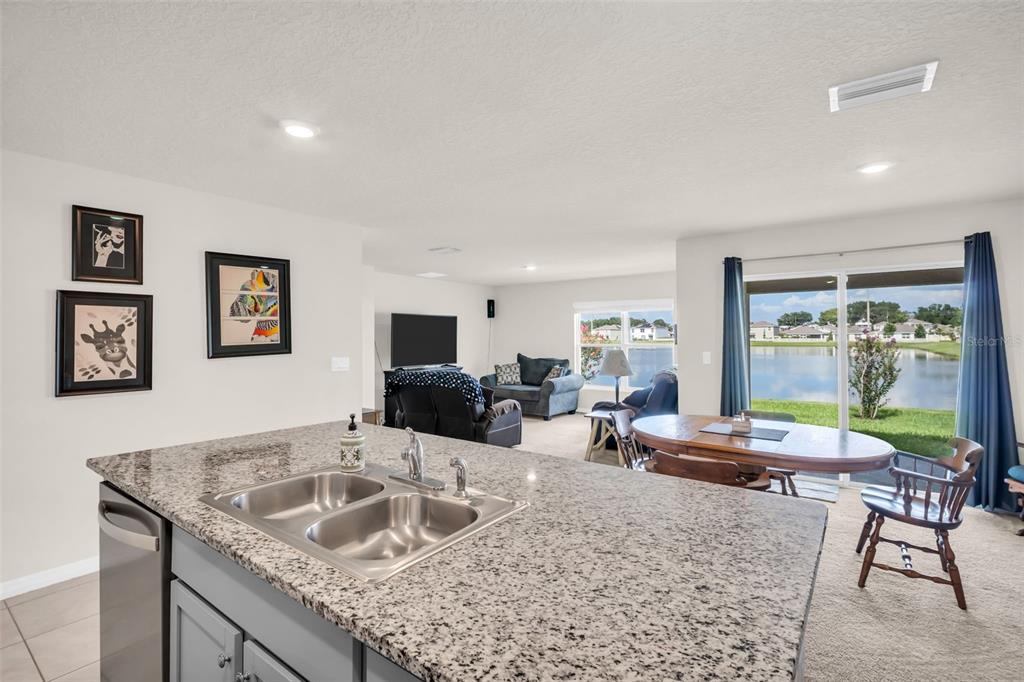 A kitchen island with a granite countertop overlooks a dining area and living room — 7774 SAIL CLOVER LANE, ZEPHYRHILLS, FL