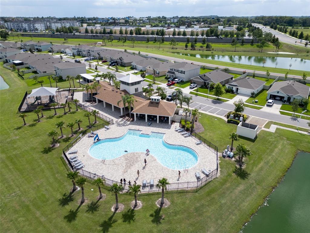An aerial view shows a community swimming pool, clubhouse, playground, and surrounding residential homes — 7774 SAIL CLOVER LANE, ZEPHYRHILLS, FL