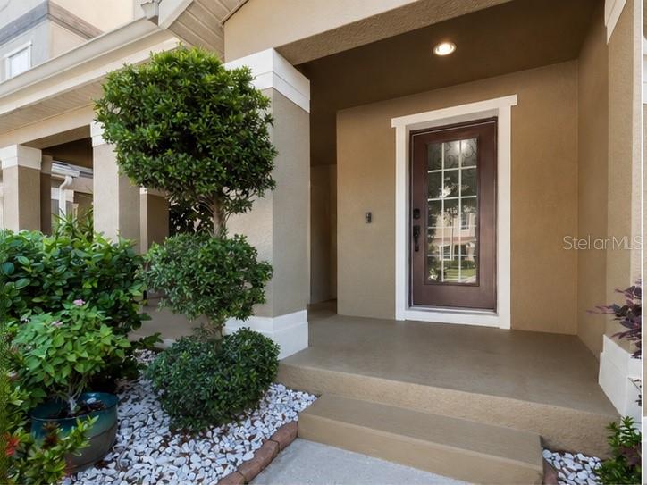A front porch with a brown door, a topiary tree, and white gravel landscaping — 10862 SUNSET RIDGE LANE, ORLANDO, FL