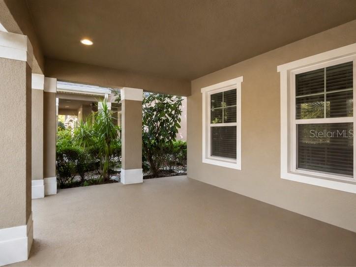 A covered patio with tan walls, white trim, and two windows overlooking outdoor landscaping — 10862 SUNSET RIDGE LANE, ORLANDO, FL