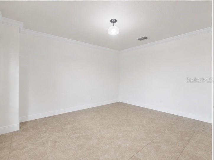 An empty room with white walls, crown molding, and light-colored tile flooring — 10862 SUNSET RIDGE LANE, ORLANDO, FL