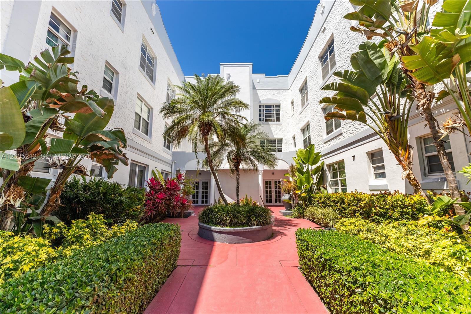 A courtyard with a red path, palm trees, and white multi-story apartment buildings — 1200 Euclid Ave # 102, Miami Beach FL 33139, MIAMI BEACH, FL