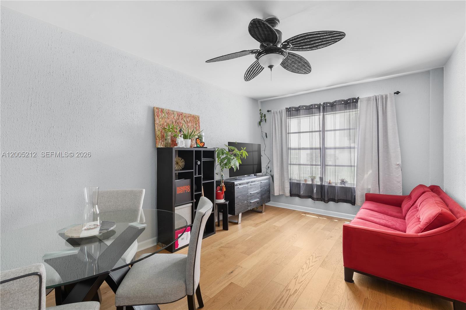 A living and dining area features light wood floors, a red sofa, and a ceiling fan — 1200 Euclid Ave # 102, Miami Beach FL 33139, MIAMI BEACH, FL