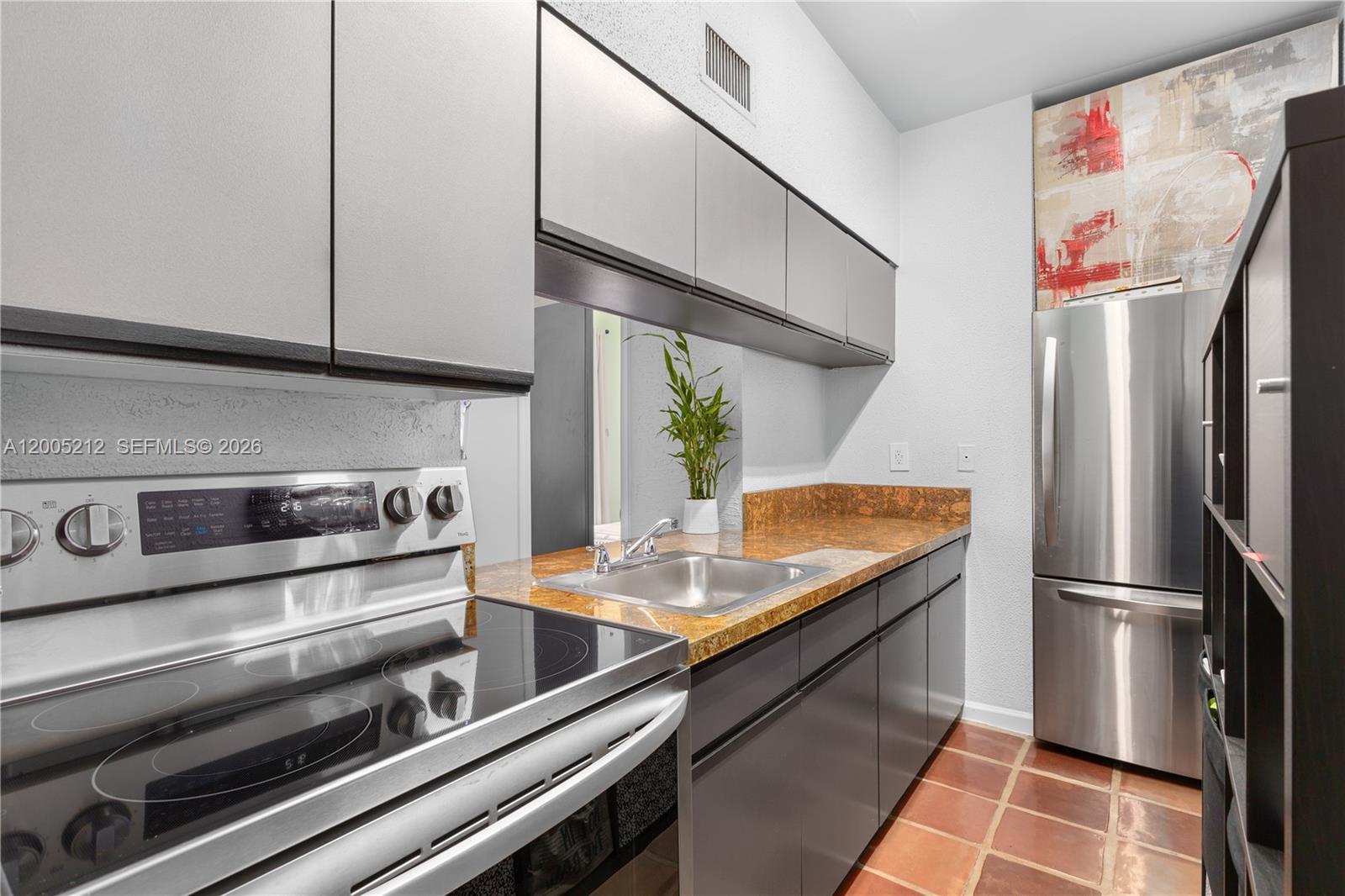 A kitchen features dark gray cabinets, a stainless steel stove, and a speckled brown countertop — 1200 Euclid Ave # 102, Miami Beach FL 33139, MIAMI BEACH, FL