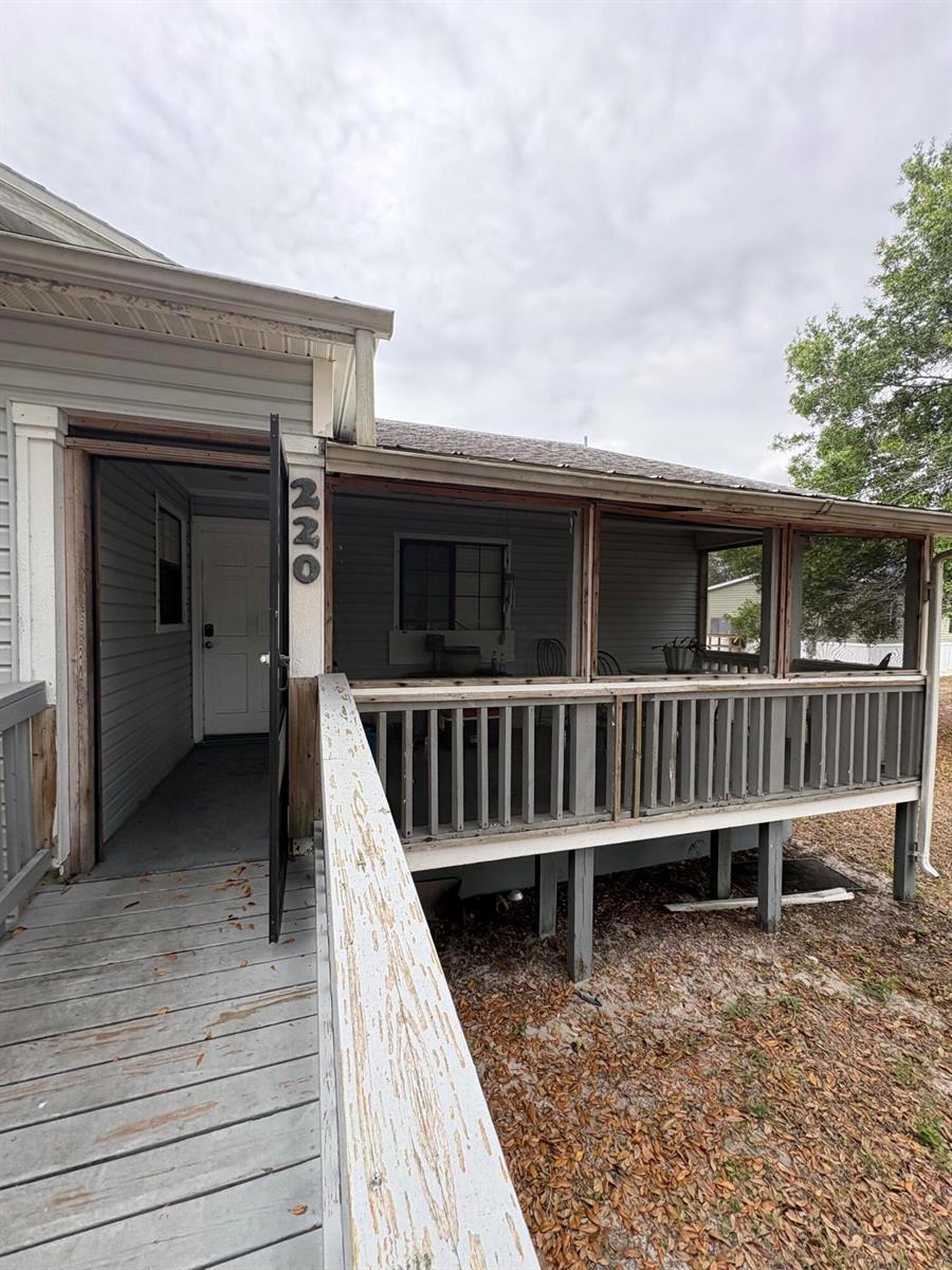 A wooden ramp leads to a screened-in porch with gray railings and a house entrance — 230 N Brida Street, Clewiston FL 33440, CLEWISTON, FL