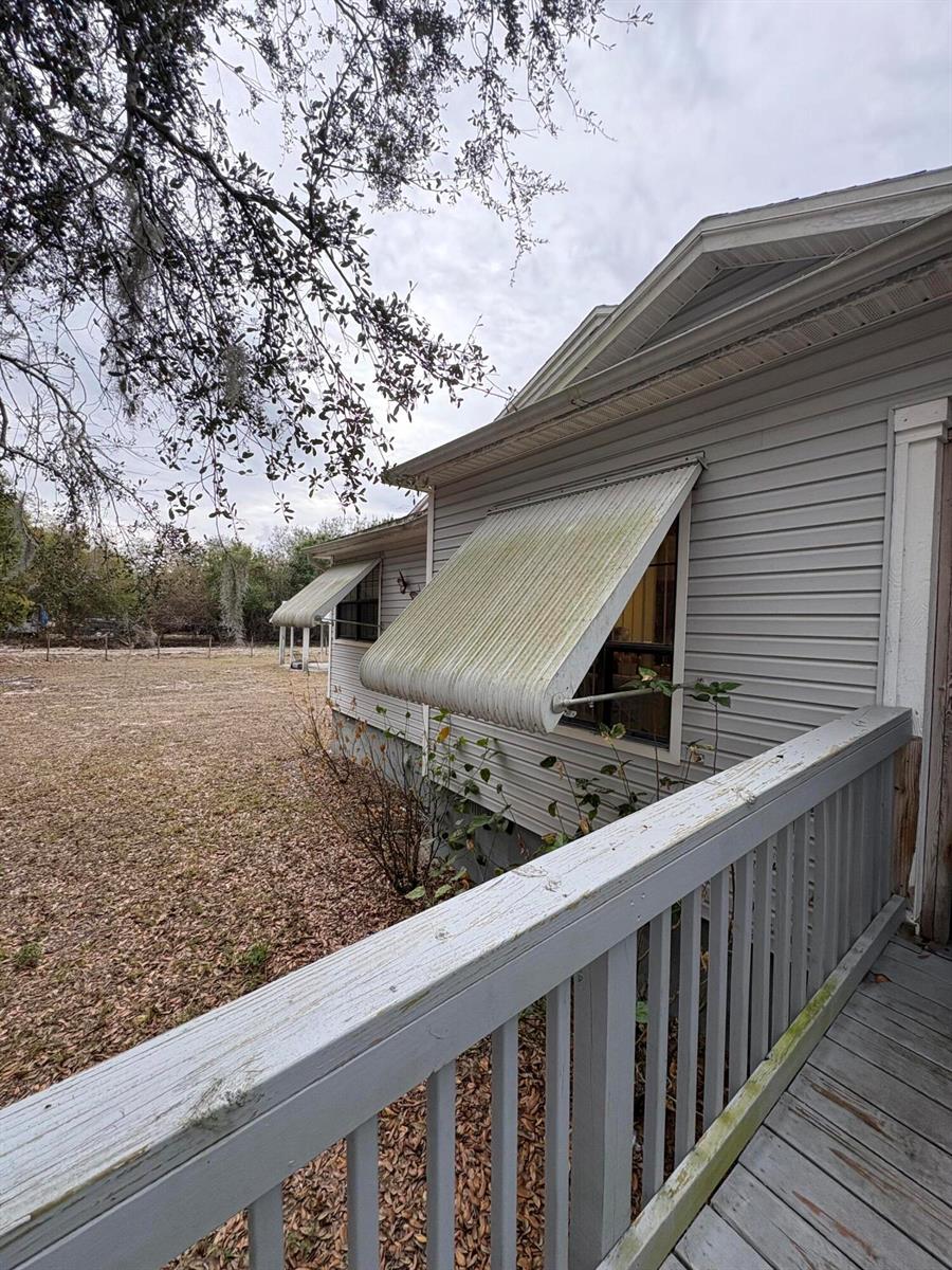 A side view of a house exterior featuring gray siding, metal window awnings, and a deck — 230 N Brida Street, Clewiston FL 33440, CLEWISTON, FL