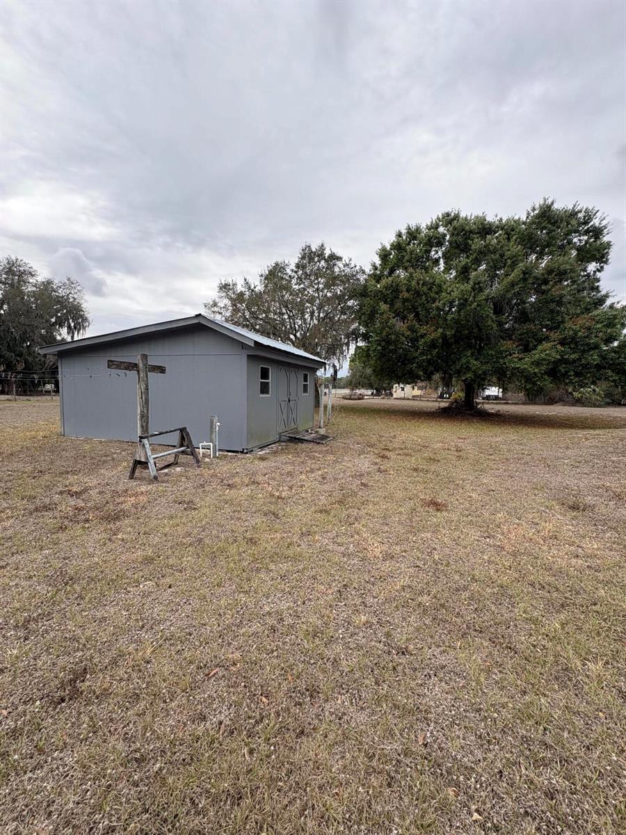A grey shed sits in a large, grassy field near a large tree — 230 N Brida Street, Clewiston FL 33440, CLEWISTON, FL