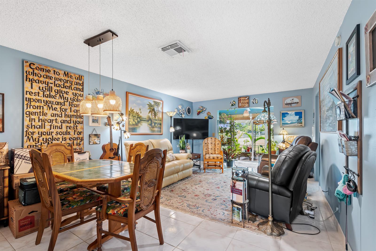 A living and dining area features light blue walls, tile flooring, and a large wall-mounted scripture sign — 2017 SW Golf Lane # 113, Boynton Beach FL 33426, BOYNTON BEACH, FL