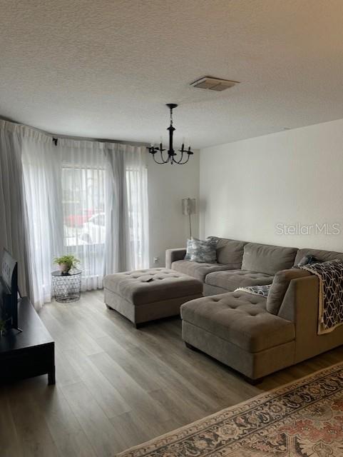A living room features a grey sectional sofa, light wood-look flooring, and a black chandelier — 4352 AQUA VISTA DRIVE UNIT 9D, ORLANDO, FL