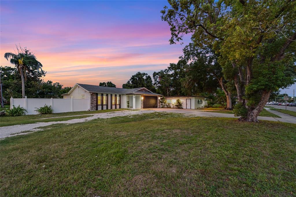 A single-story house with a white fence, a gravel driveway, and a large tree at sunset — 11635 131ST STREET, LARGO, FL