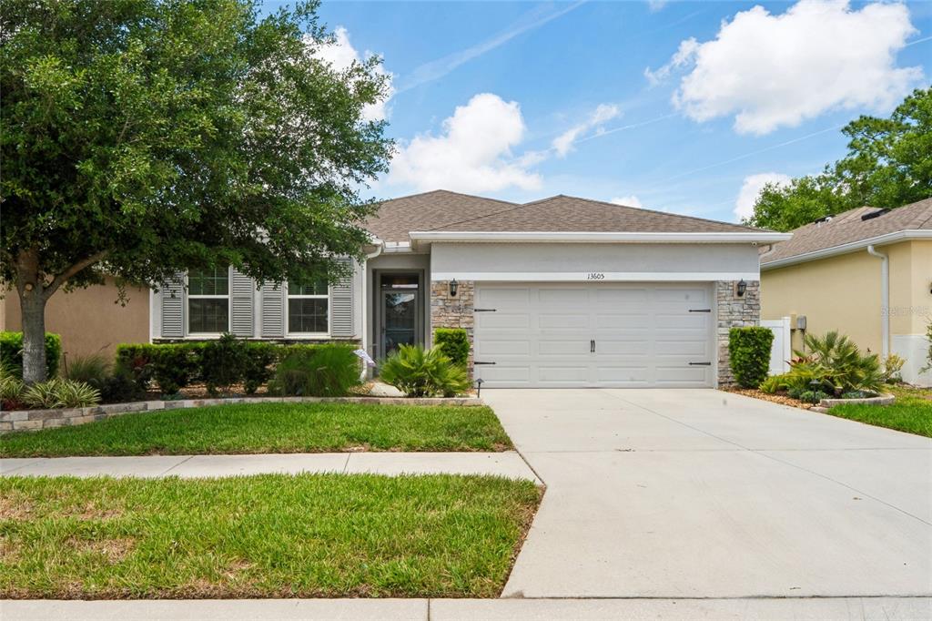 A single-story house with a two-car garage, stone accents, and a landscaped front yard — 13605 PADDINGTON WAY, SPRING HILL, FL