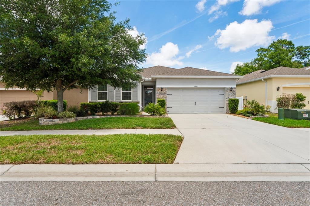 A single-story suburban house features a two-car garage, stone accents, and a large front tree — 13605 PADDINGTON WAY, SPRING HILL, FL