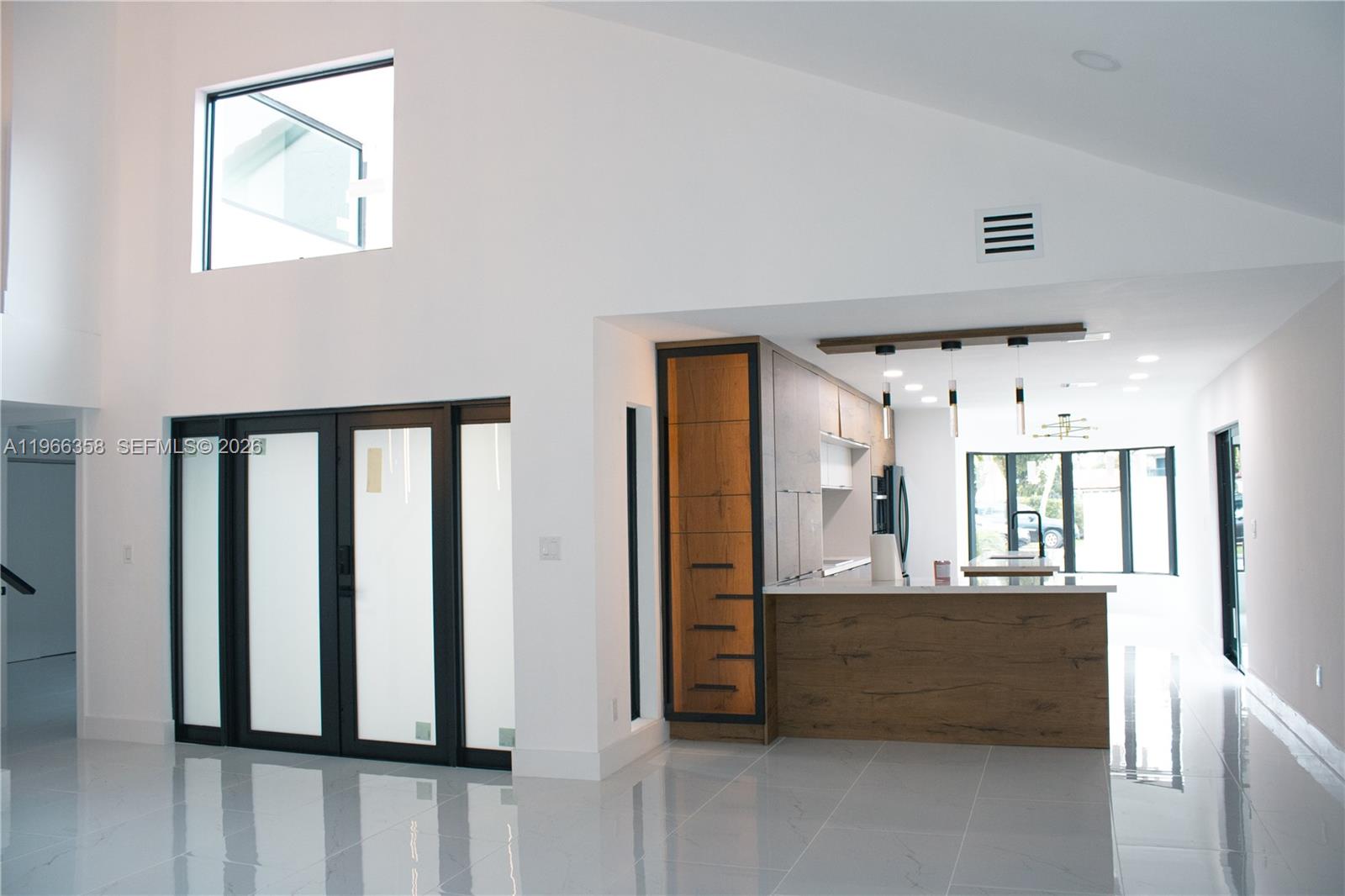 A modern kitchen with wood-toned cabinetry and a white island sits beside a glass-paned door — 10433 SW 118th Ct, Miami FL 33186, MIAMI, FL