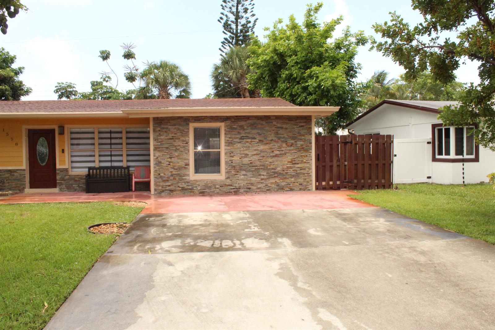 A single-story house with a stone facade, a concrete driveway, and a wooden privacy fence — 1558 NE 30th Street, Pompano Beach FL 33064, POMPANO BEACH, FL