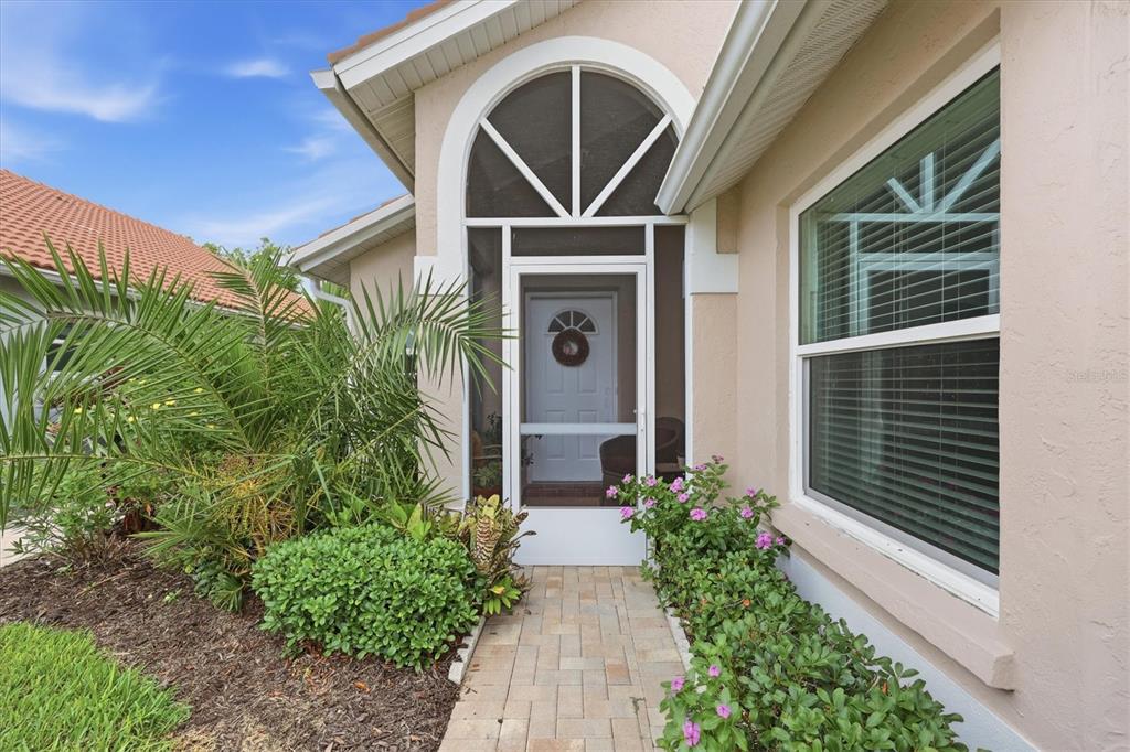 A paved walkway leads to a screened front entryway with a palm tree and landscaping — 1468 TURNBERRY DRIVE, VENICE, FL