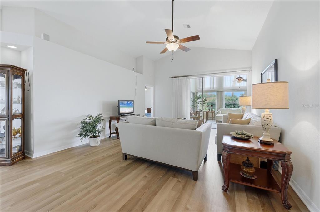 A living room with light wood flooring, a ceiling fan, and a view of a sunroom — 1468 TURNBERRY DRIVE, VENICE, FL