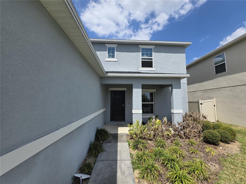 A two-story gray house features a covered entryway, a dark front door, and landscaping — 5721 SAGUNTO DRIVE, DAVENPORT, FL