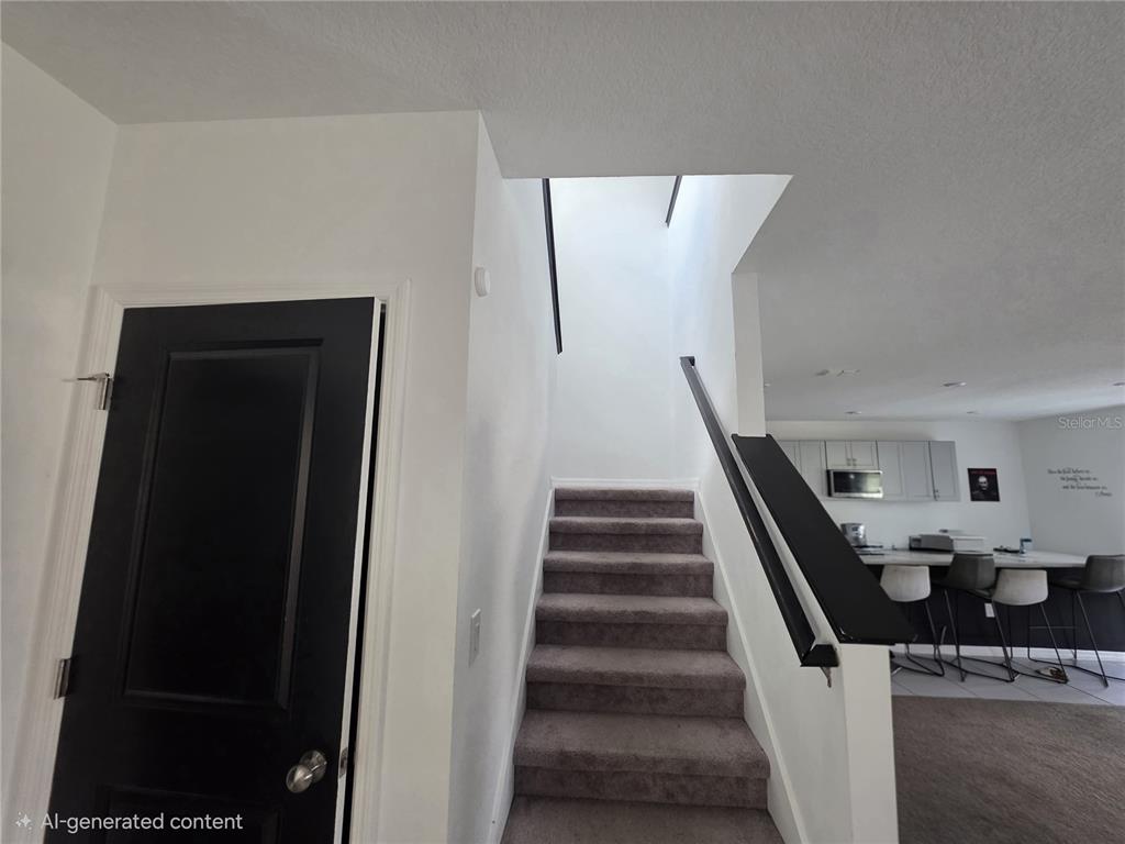 This image shows a carpeted staircase leading upward next to a black door and kitchen — 5721 SAGUNTO DRIVE, DAVENPORT, FL