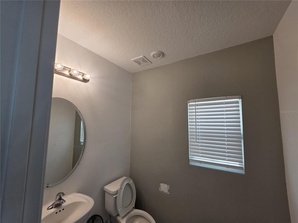 A small bathroom features a pedestal sink, a round mirror, and a window with blinds — 5721 SAGUNTO DRIVE, DAVENPORT, FL