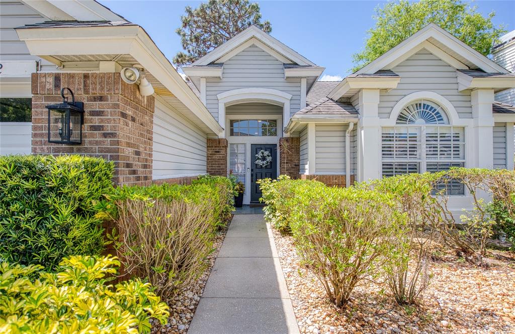 A concrete walkway leads to the front entrance of a house with light-colored siding — 2182 TREVOR ROAD, PALM HARBOR, FL