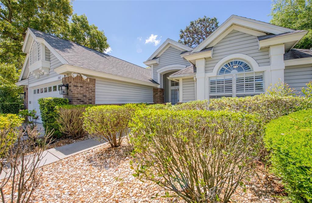 A light gray house with a brick accent wall, a garage, and landscaped front yard — 2182 TREVOR ROAD, PALM HARBOR, FL