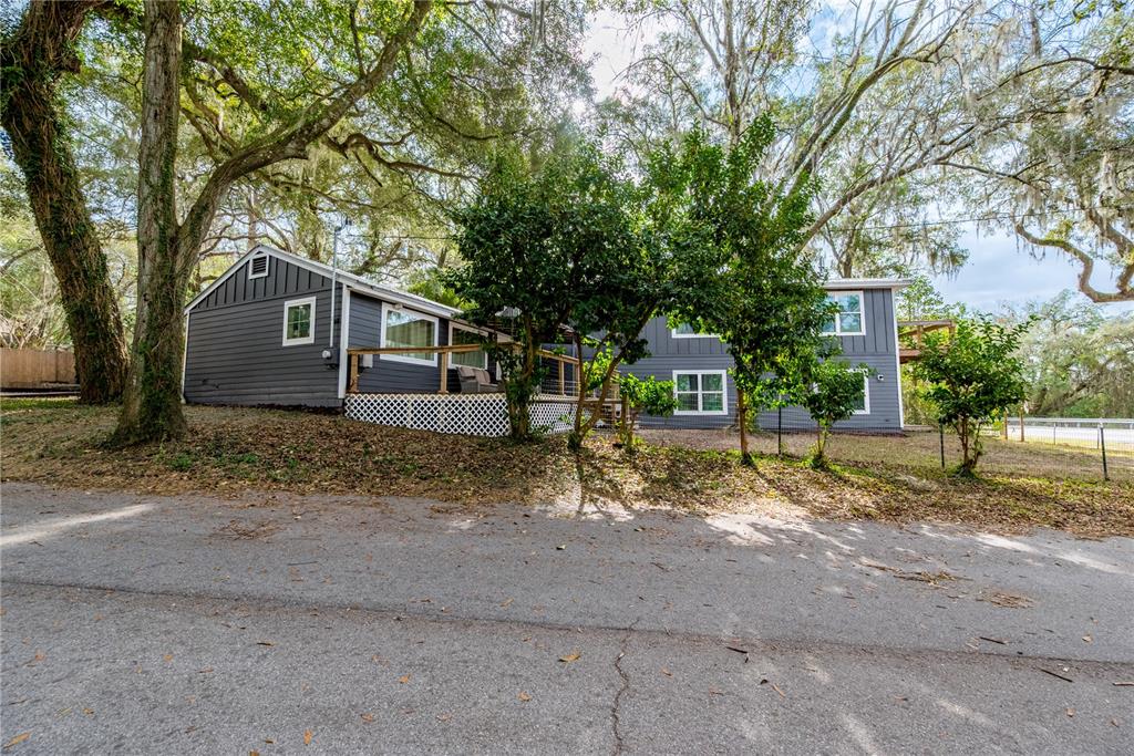 A two-story gray house with a wooden deck sits on a sloped, tree-covered lot — 1353 CHATAUQUA WAY, KEYSTONE HEIGHTS, FL