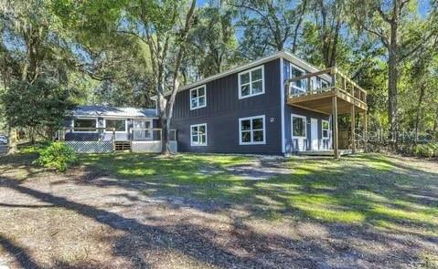A two-story dark blue house with a wooden deck stands among trees on a lawn — 1353 CHATAUQUA WAY, KEYSTONE HEIGHTS, FL