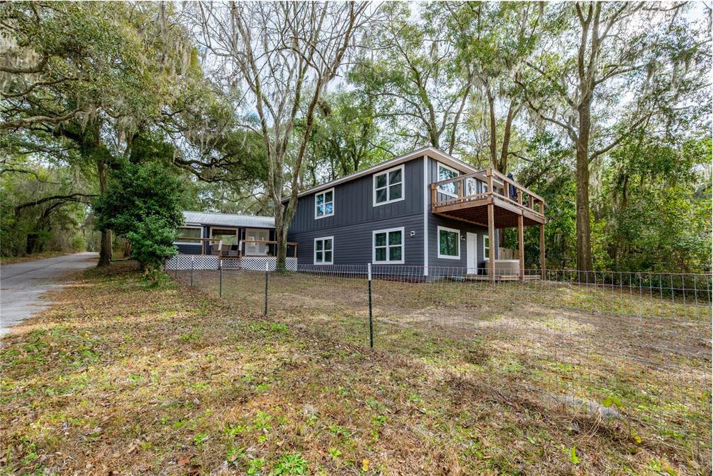 A two-story dark gray house with a wooden deck sits among trees behind a fence — 1353 CHATAUQUA WAY, KEYSTONE HEIGHTS, FL