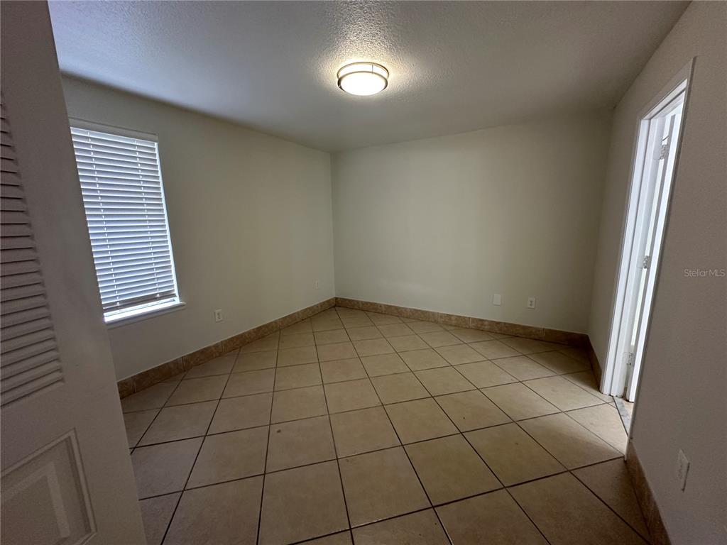 An empty room features beige tile flooring, white walls, a window with blinds, and lighting — 1000 DOLPHIN DRIVE, WINTER GARDEN, FL