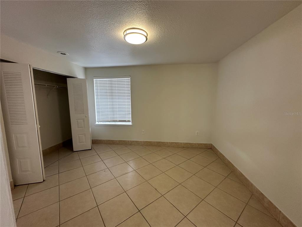 An empty bedroom features beige tile flooring, white walls, a closet, and a window — 1000 DOLPHIN DRIVE, WINTER GARDEN, FL