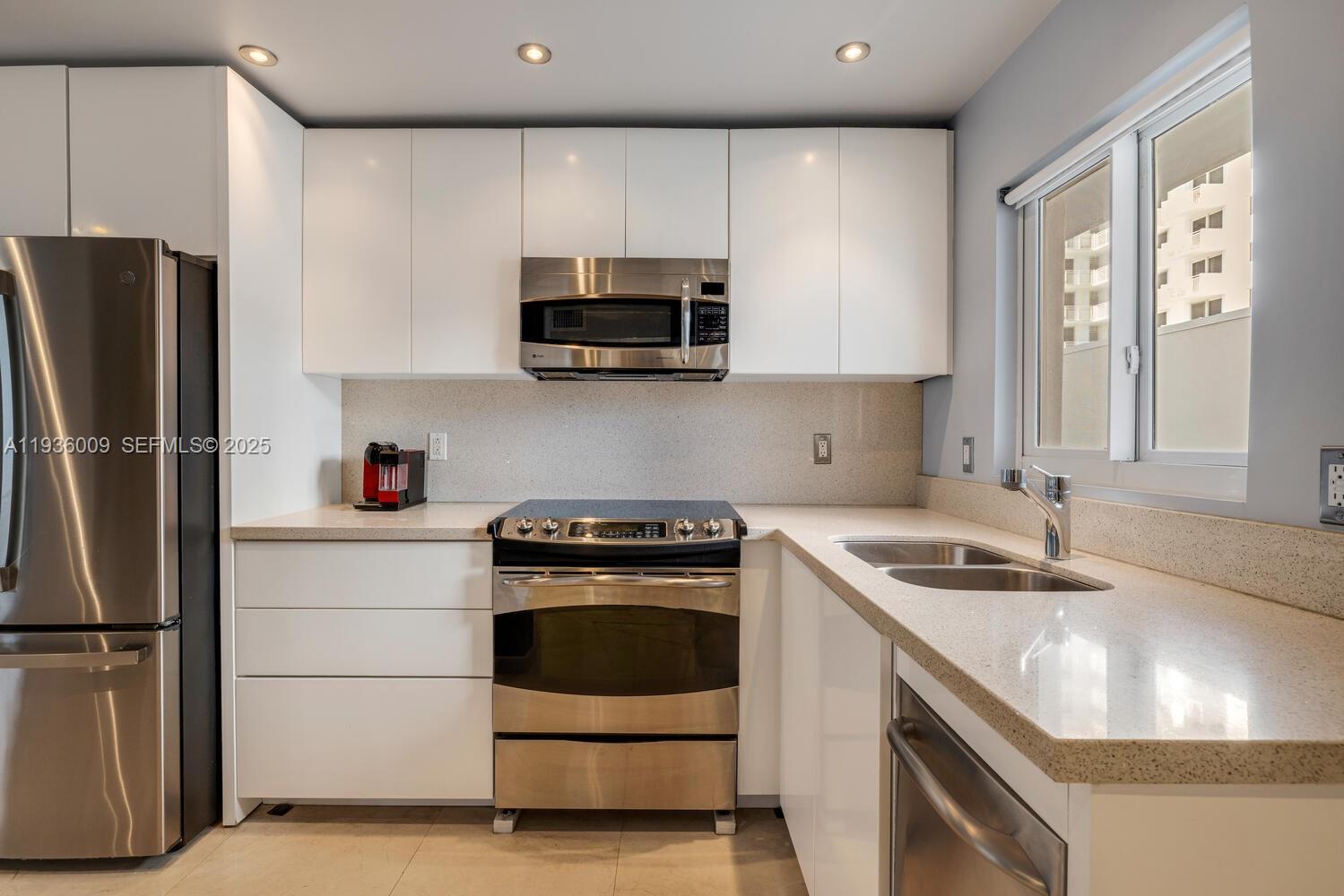 A modern kitchen features white cabinets, stainless steel appliances, and light-colored stone countertops — 325 Ocean Dr # 409, Miami Beach FL 33139, MIAMI BEACH, FL