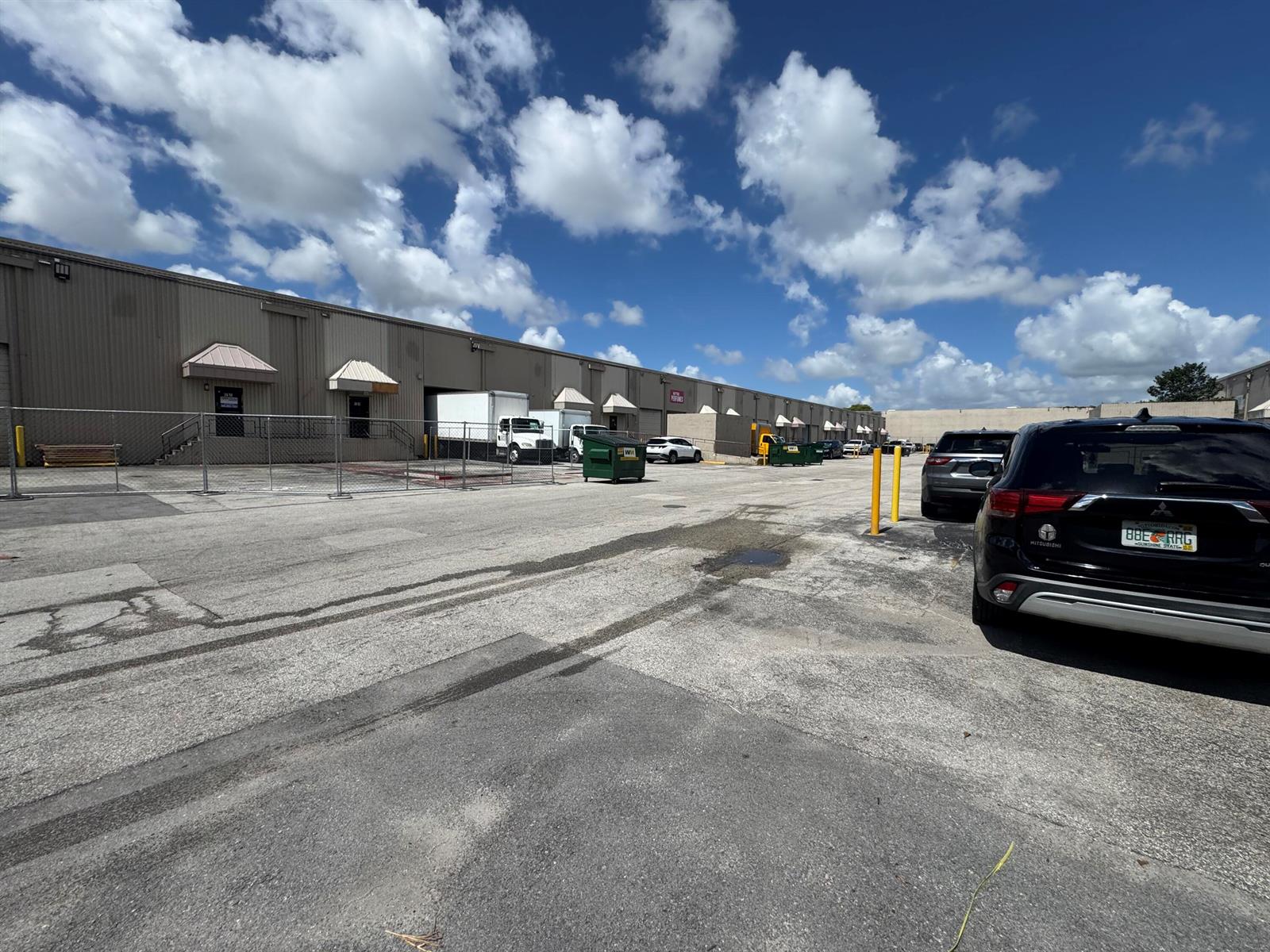 A parking lot in front of a long, single-story industrial warehouse building under a blue sky — 2710 NW 72nd Avenue, Miami FL 33122, MIAMI, FL