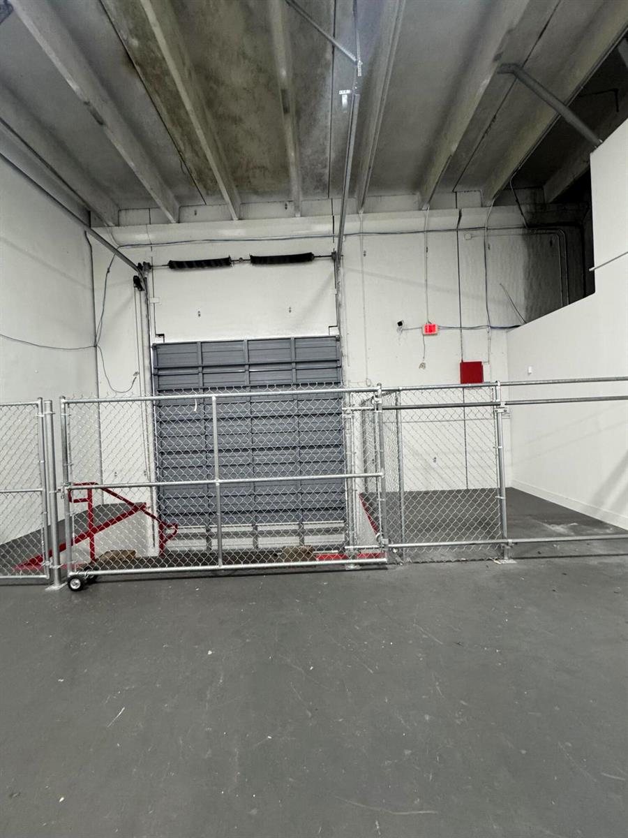 A warehouse interior features a gray roll-up door enclosed by a chain-link fence — 2710 NW 72nd Avenue, Miami FL 33122, MIAMI, FL