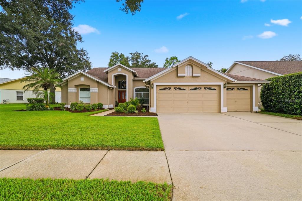 A single-story suburban house with a tan stucco exterior, a three-car garage, and a lawn — 28331 OPENFIELD LOOP, WESLEY CHAPEL, FL