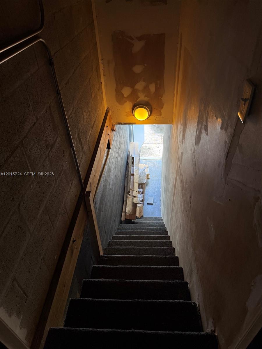 A narrow, carpeted staircase leads down toward an exterior doorway with stacked construction materials — 1775 Blount Rd # 410, Pompano Beach FL 33069, POMPANO BEACH, FL