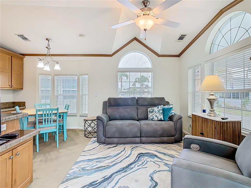 A living room and dining area with a vaulted ceiling, ceiling fan, and large windows — 9000 US HWY 192 UNIT 324, CLERMONT, FL